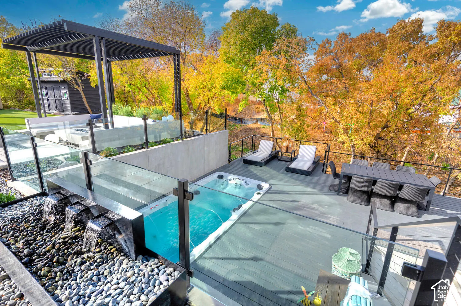 Multi-level exterior deck featuring a swim spa, custom rock water feature, glass railing systems, and a louvered metal pergola