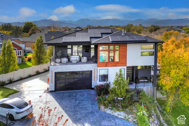 Modern exterior featuring a stacked stone facade, wood-paneled accents, roof-mounted solar panels, an elevated balcony, and a multi-car garage with a frosted glass door