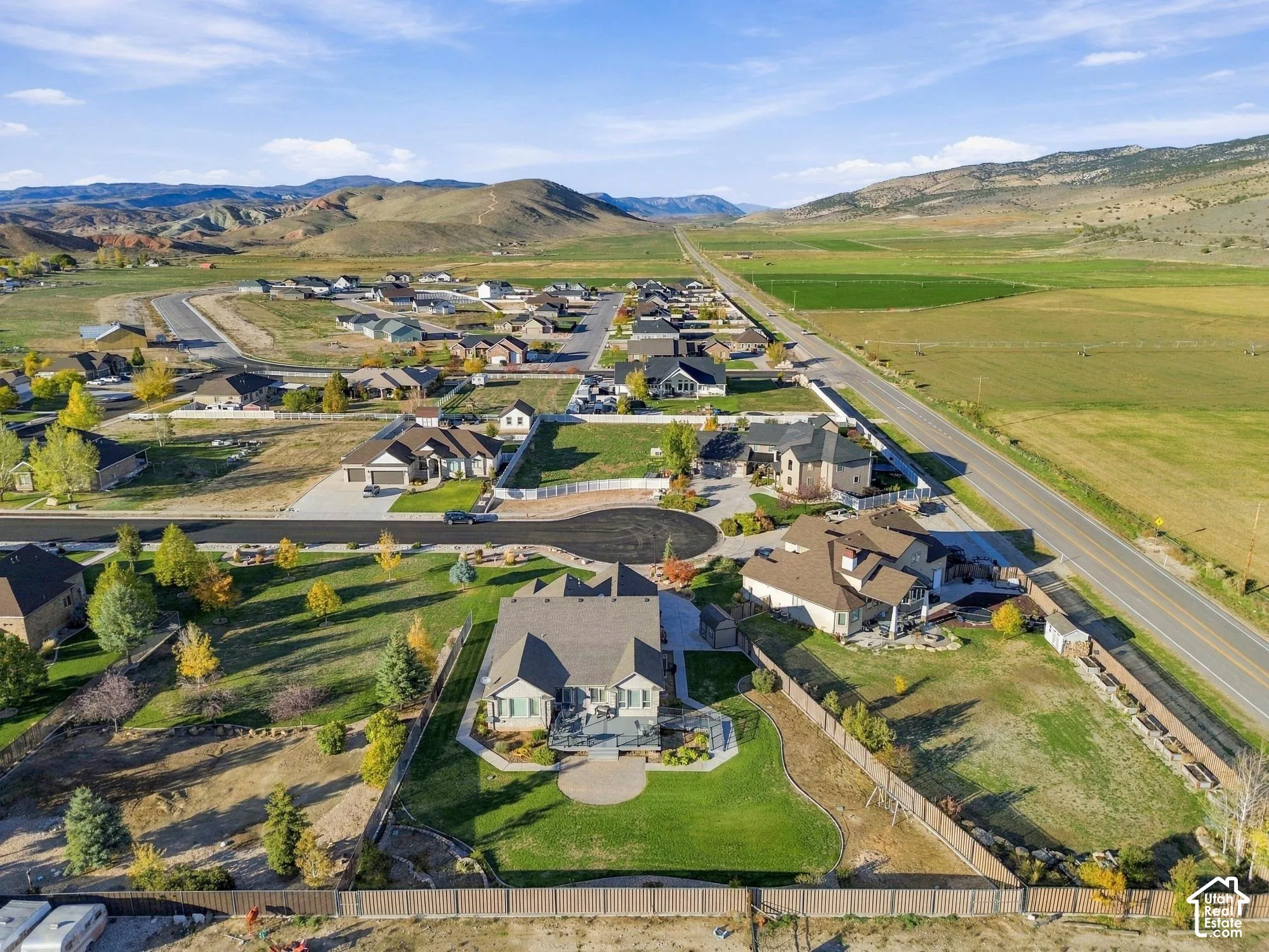 Aerial perspective showcasing a residential property with a landscaped lawn, paved patio, perimeter fencing, and mountain backdrop