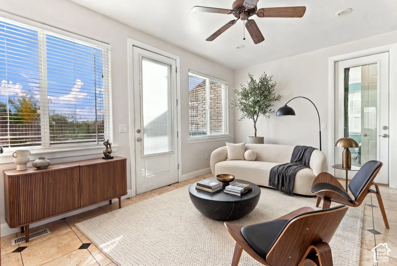 Tile flooring with decorative inlays, large windows with horizontal blinds, ceiling fan with integrated lighting, and a glass-paneled exterior door