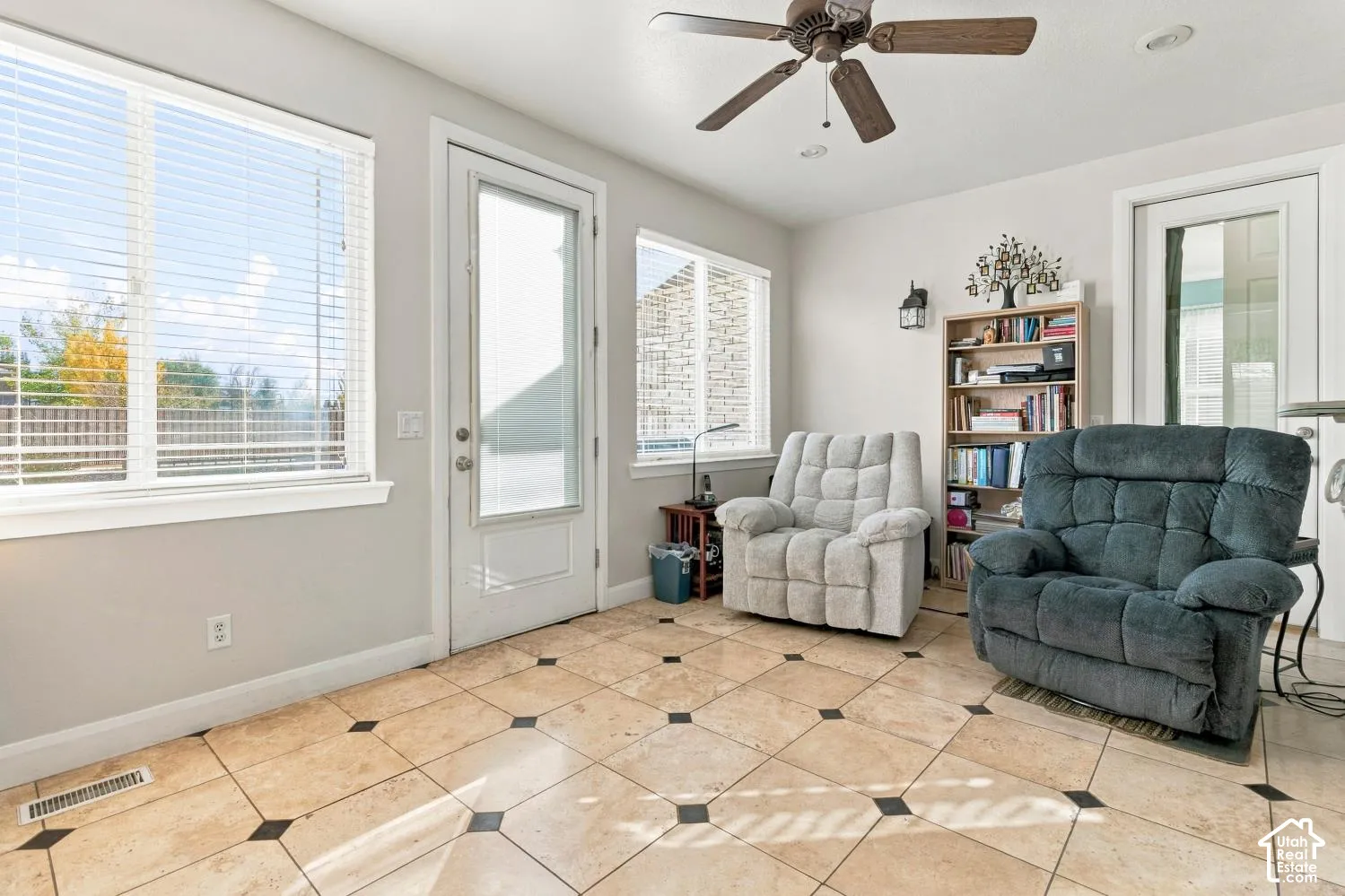 Light-filled room featuring large windows, stone-finish tile flooring with decorative inserts, a full-lite glass exterior door, and a ceiling fan with integrated lighting