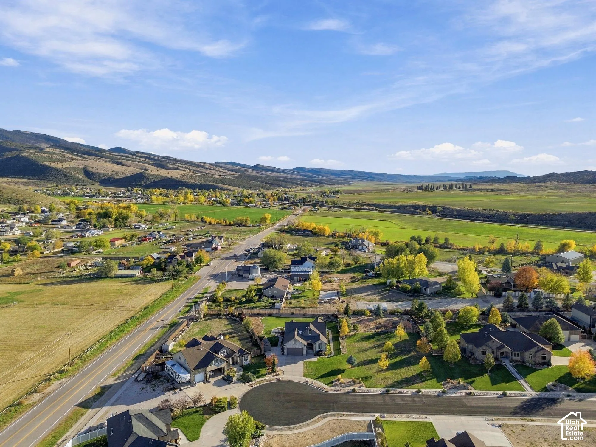 Aerial perspective featuring expansive mountain terrain, open pastures, and residential properties situated along a paved thoroughfare
