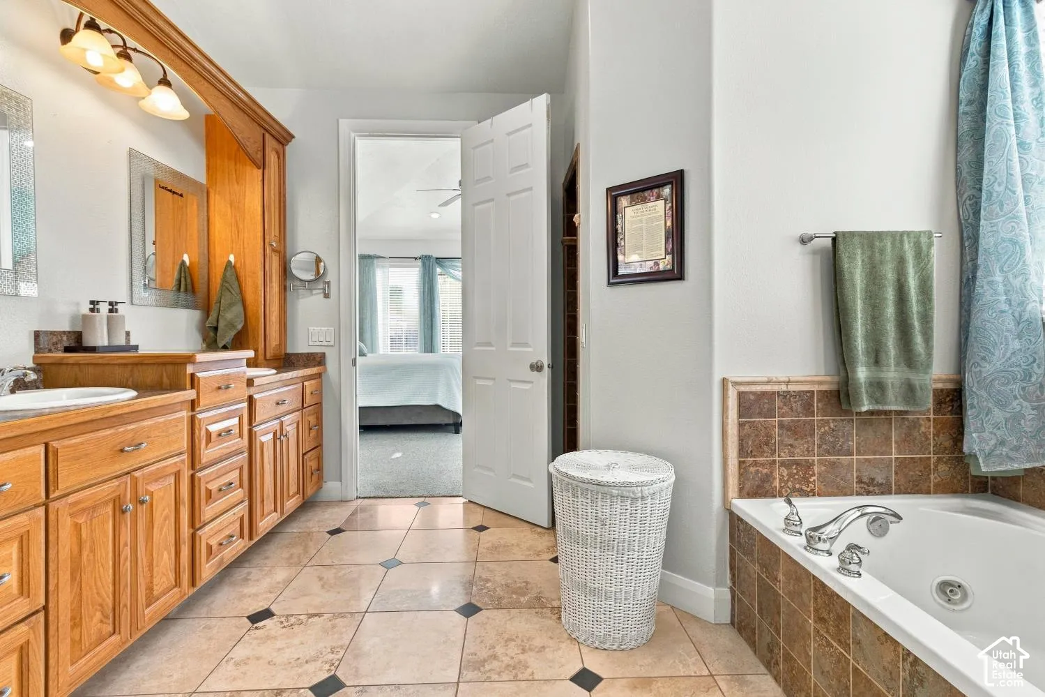 Bathroom featuring wood-finish cabinetry, a drop-in soaking tub with a tiled surround, dual integrated sinks, and stone-tile flooring with decorative insets