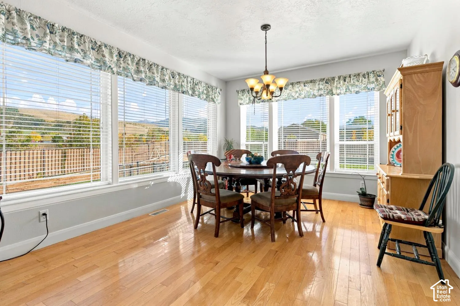 Light-filled room featuring polished wood-finish flooring, an array of windows with blinds, a multi-light metal chandelier, and mountain scenery