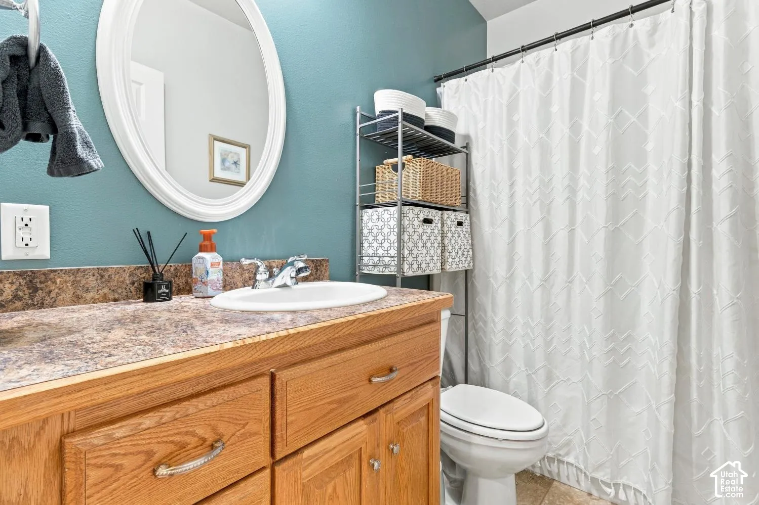 Bathroom vanity featuring natural wood cabinetry, integrated countertop with a drop-in sink, chrome hardware, oval wall-mounted mirror, and a shower-tub combination with a curtain rod