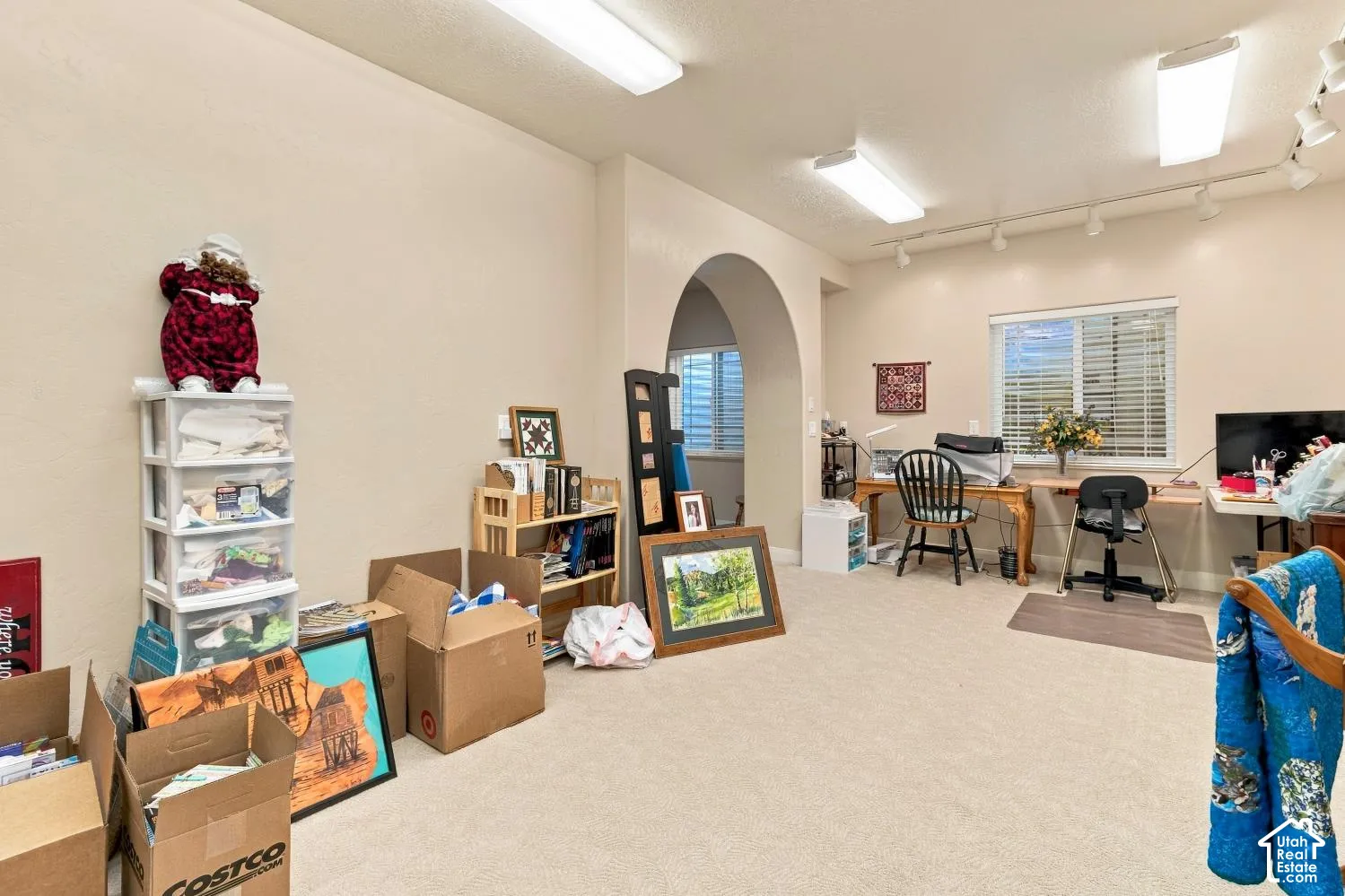 Neutral-toned interior space featuring an arched entryway, recessed track lighting, flush-mount fluorescent ceiling fixtures, and a single-hung window with horizontal blinds