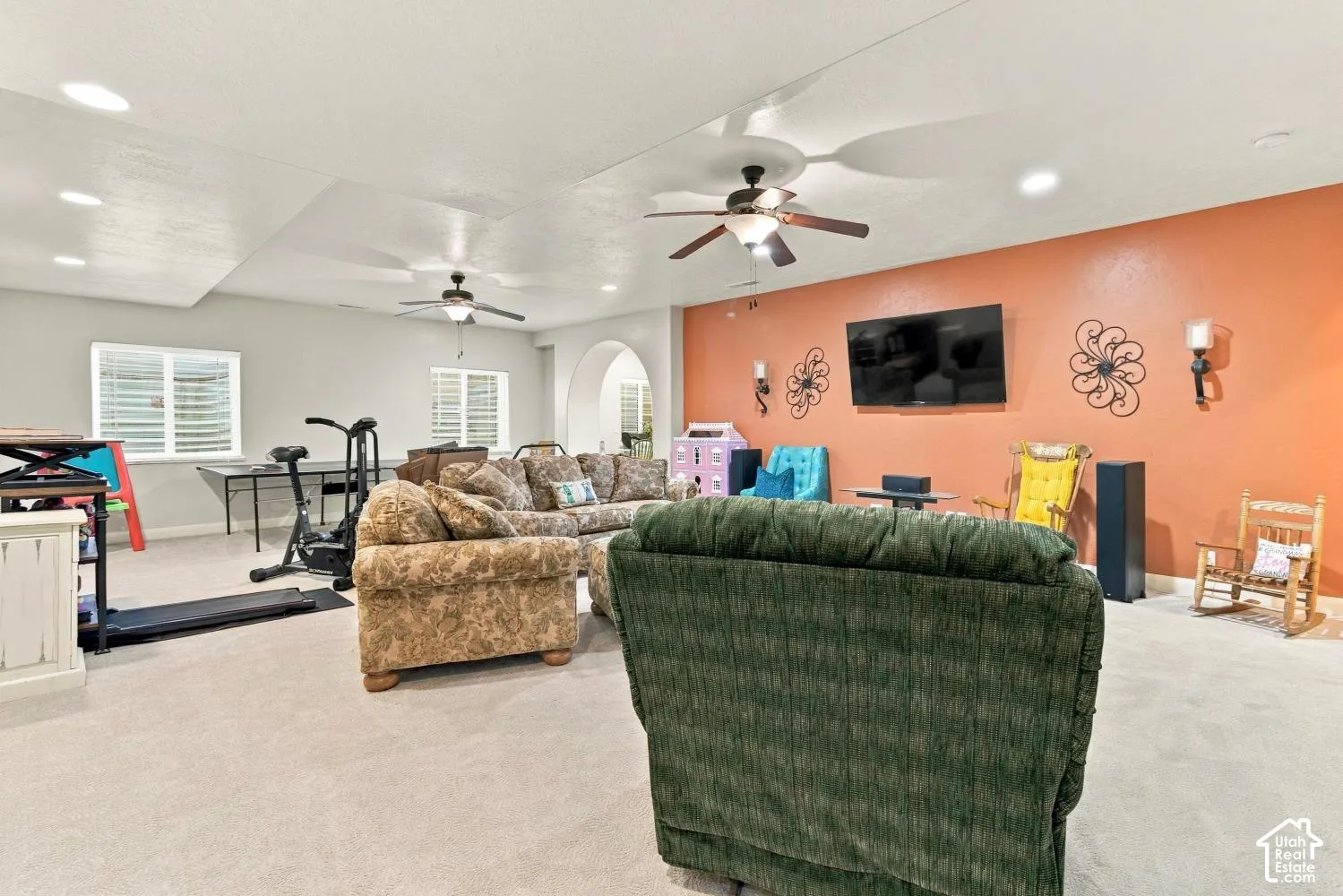 Neutral-toned interior space featuring recessed lighting, dual ceiling fans, wall-mounted light fixtures, and a prominent arched entryway