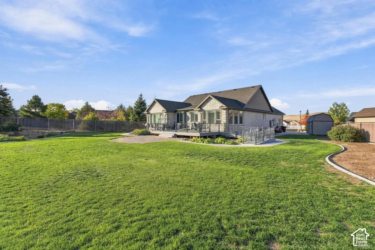 Expansive backyard featuring a manicured lawn, tiered paver patio, elevated deck with railing, and an exterior storage shed