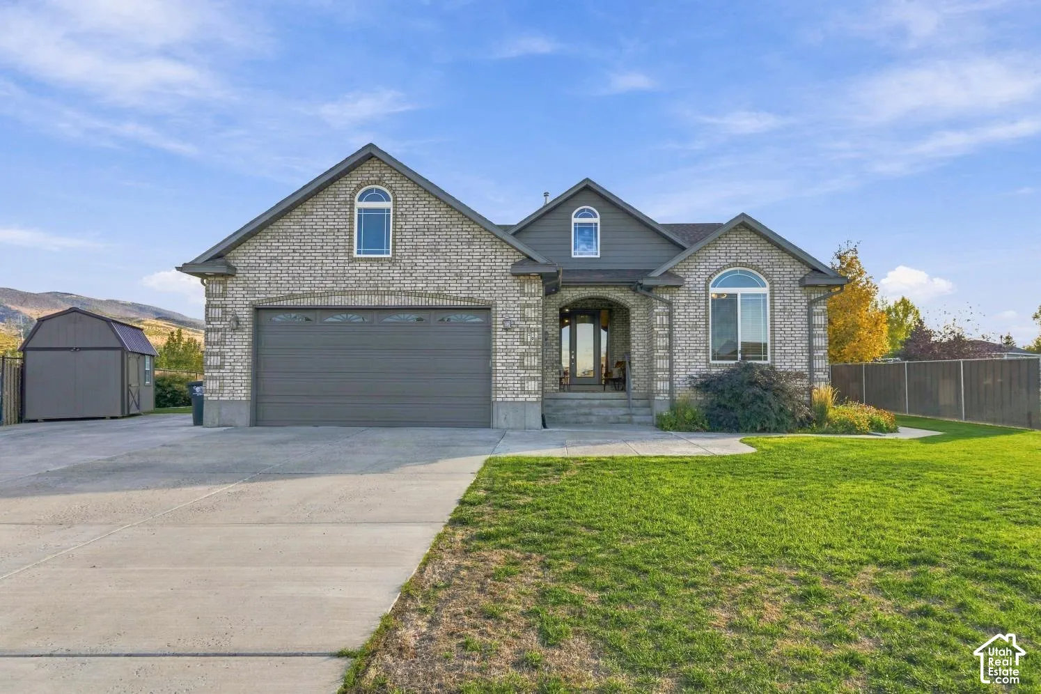 Brick exterior featuring a multi-gabled roofline, an arched entryway, a double-car garage, and a detached storage structure
