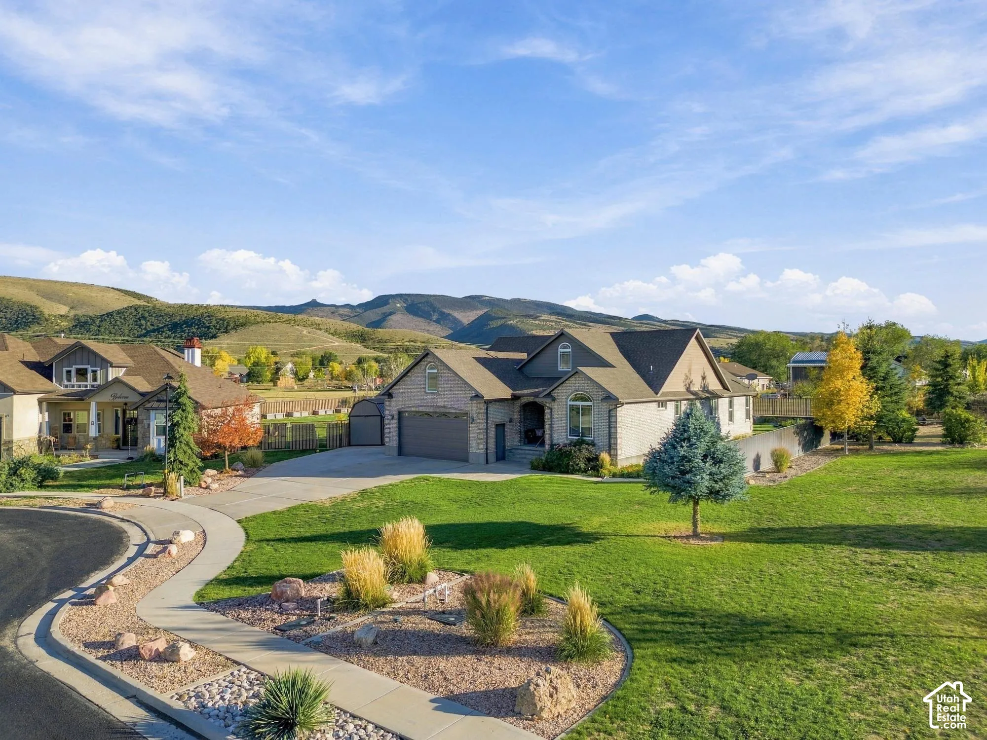 Multi-gabled brick and stone exterior with an attached garage, situated on a sprawling corner lot with mature landscaping and mountain scenery