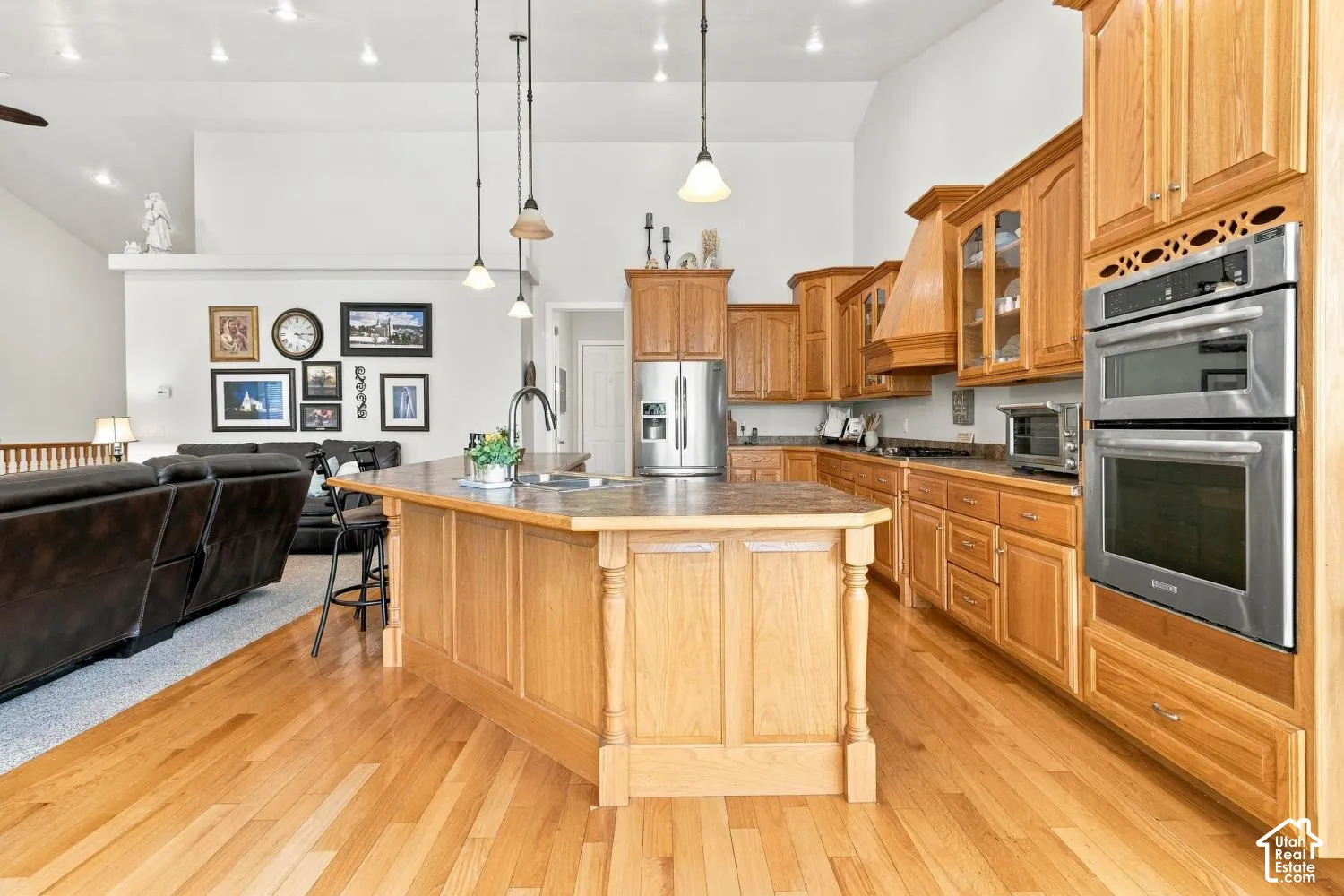 Kitchen featuring oak cabinetry, an island with countertop seating, stainless steel double wall ovens, wood-finish flooring, and vaulted ceilings