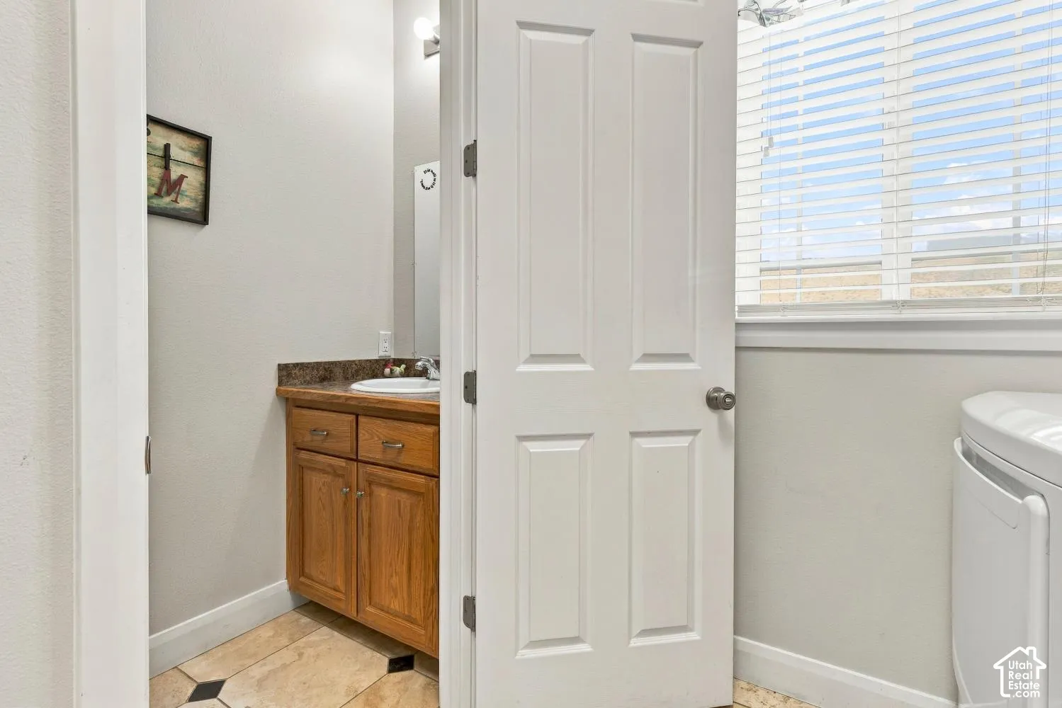 Vanity featuring a stone-composite countertop, integrated sink, and wood-finish cabinetry, complemented by tile flooring with decorative inlay and horizontal window blinds