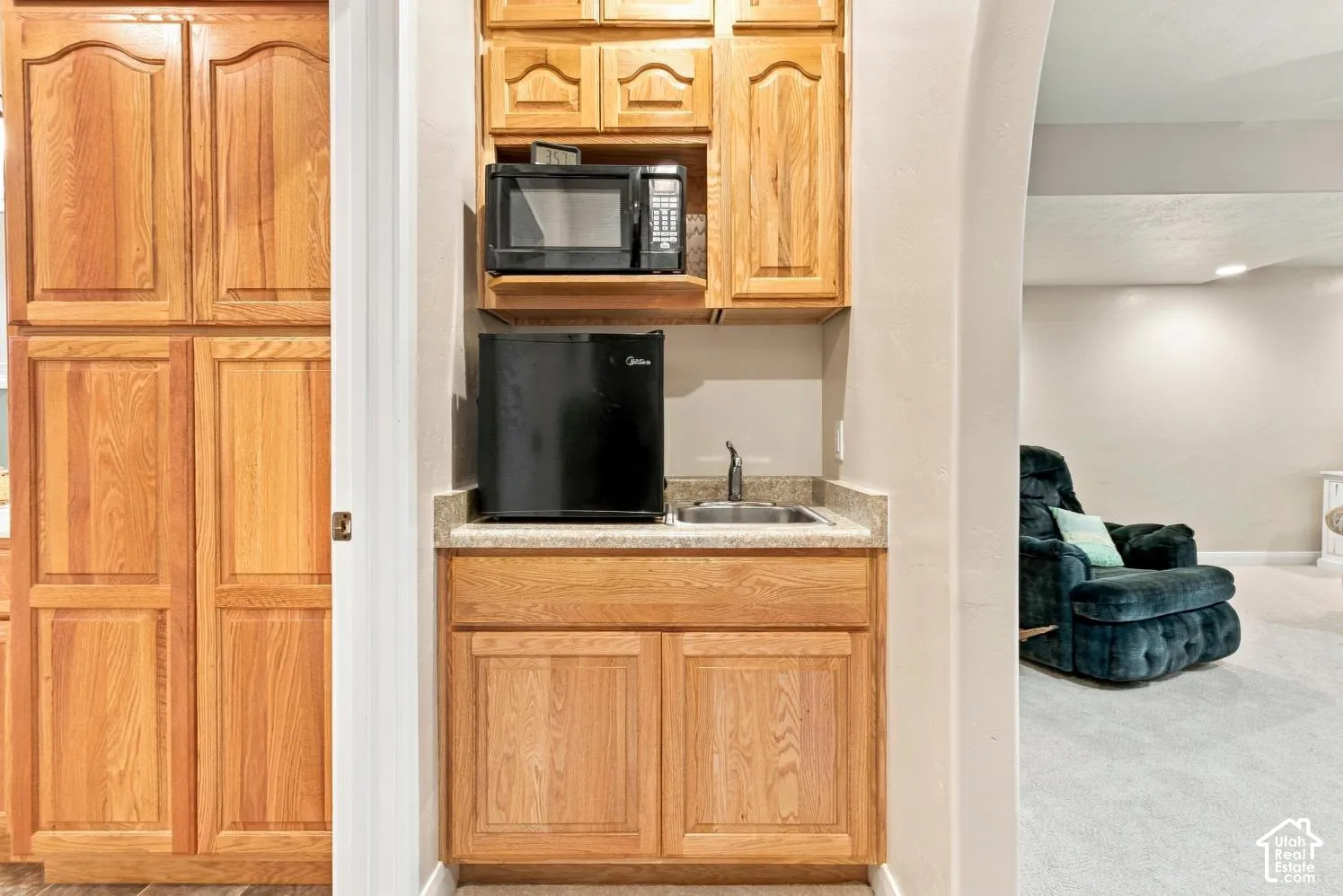 Wet bar featuring natural wood cabinetry, stone-finish countertop, stainless steel drop-in sink, and arched wall detailing