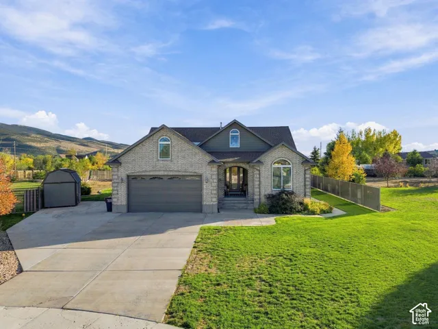 Exterior featuring brick and siding facade, an arched entryway, multiple gabled rooflines, an attached two-car garage, and a expansive lawn with perimeter fencing