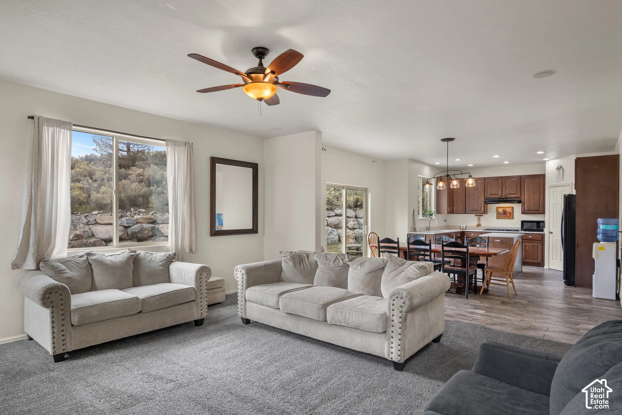Open-concept living space featuring wood-finish flooring, a multi-blade ceiling fan, recessed lighting, and kitchen cabinetry with a decorative pendant fixture