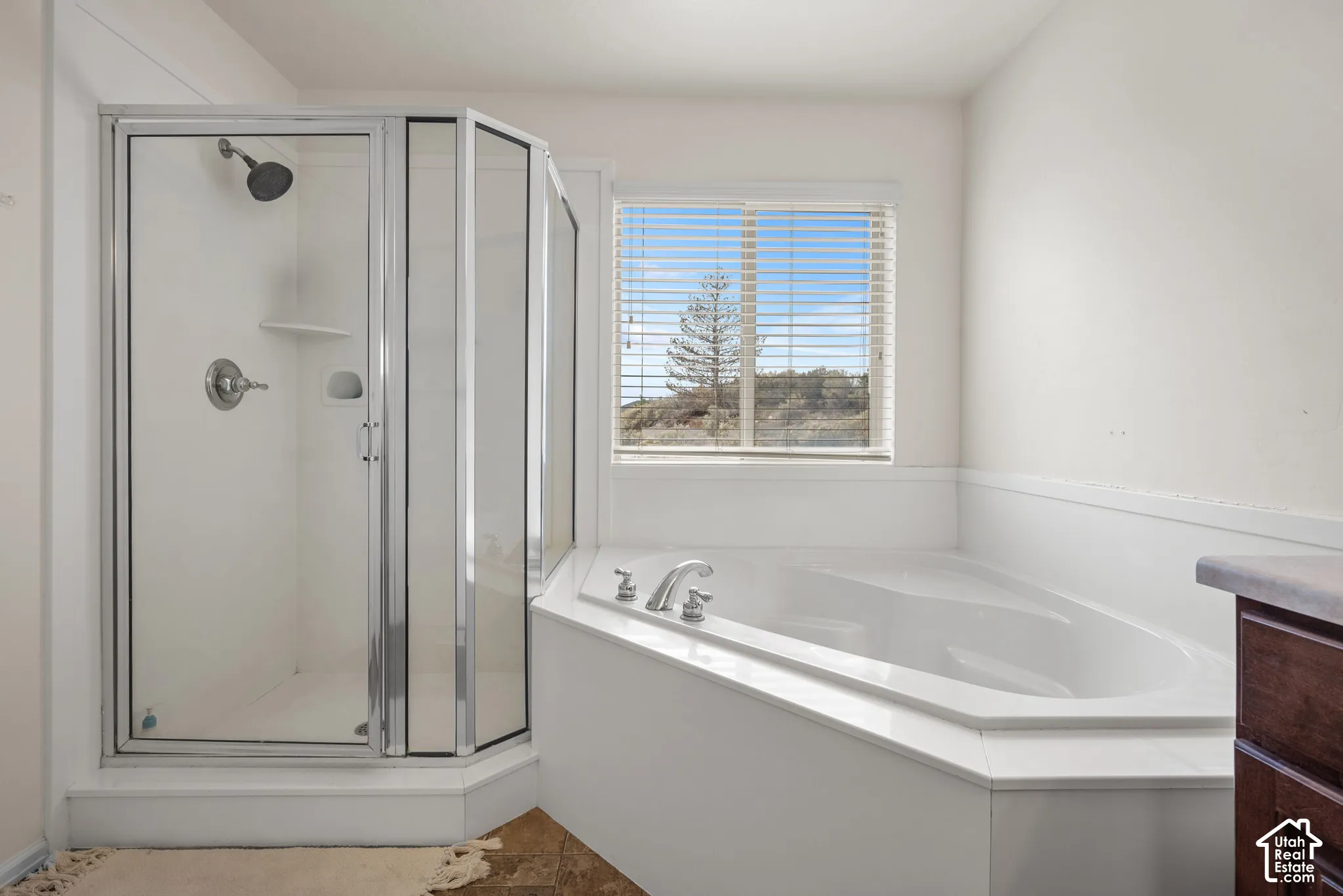 Corner shower enclosure with glass doors and polished chrome fixtures, white porcelain jetted soaking tub with a tiled surround, and a window with horizontal blinds