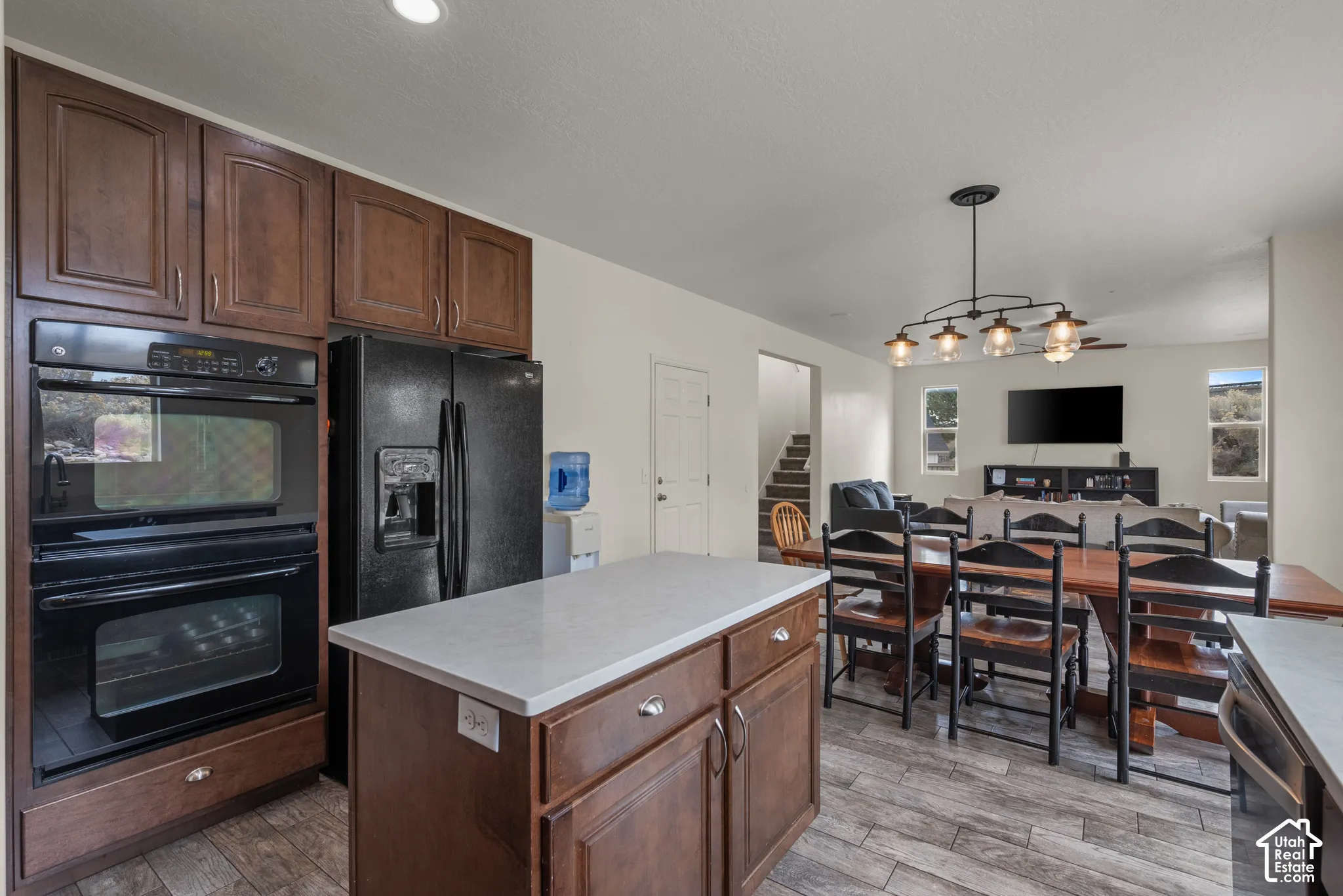 Kitchen featuring dark wood-finish cabinetry, a central island with a solid-surface countertop, built-in double ovens, and wood-finish flooring