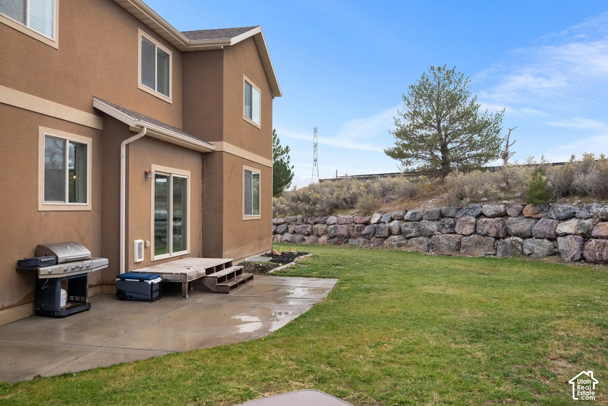 Exterior backyard featuring a concrete patio, wood-deck platform, and a tiered natural stone retaining wall