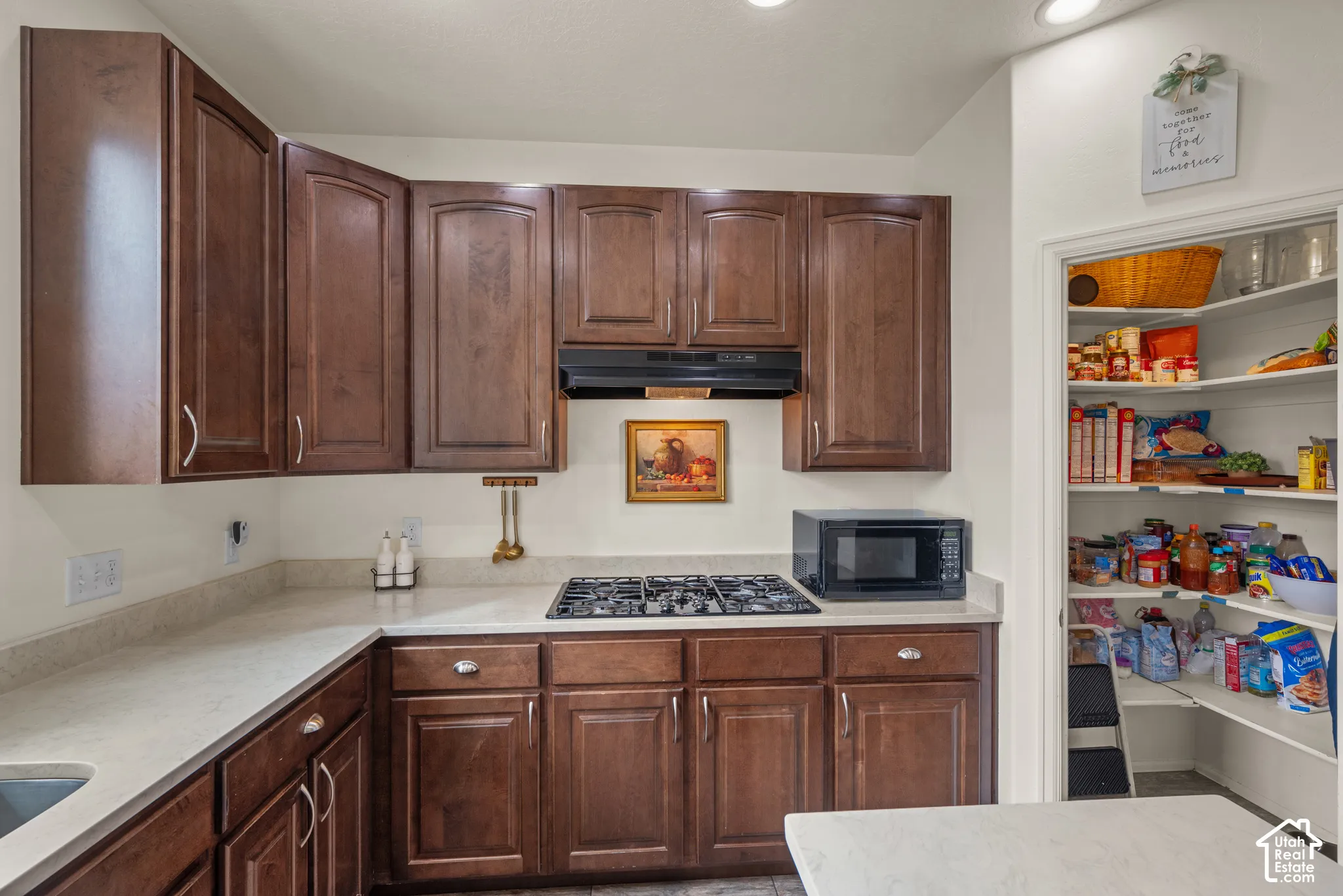 Kitchen featuring stained wood cabinetry, light-toned stone-finish countertops, a built-in gas cooktop, and an integrated walk-in pantry