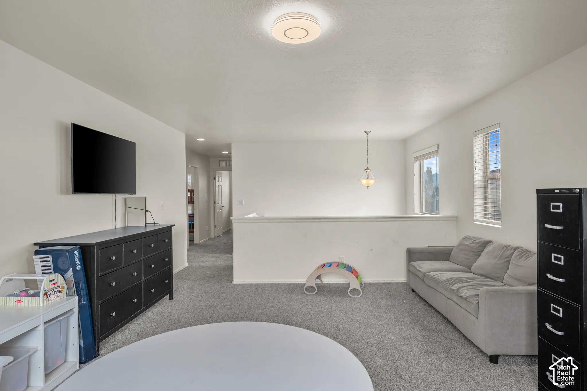 Open concept space featuring neutral wall paint, carpeting, recessed ceiling lighting, a pendant fixture, and a partial-height wall divider