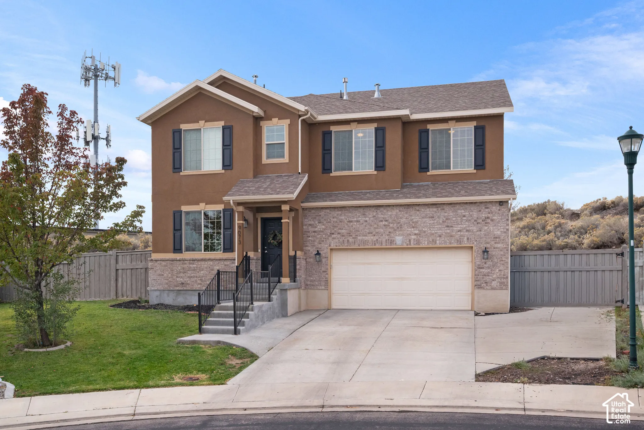 Two-story residence featuring a partial stone veneer facade, stucco exterior finish, attached two-car garage, concrete driveway, and front entryway with metal railings