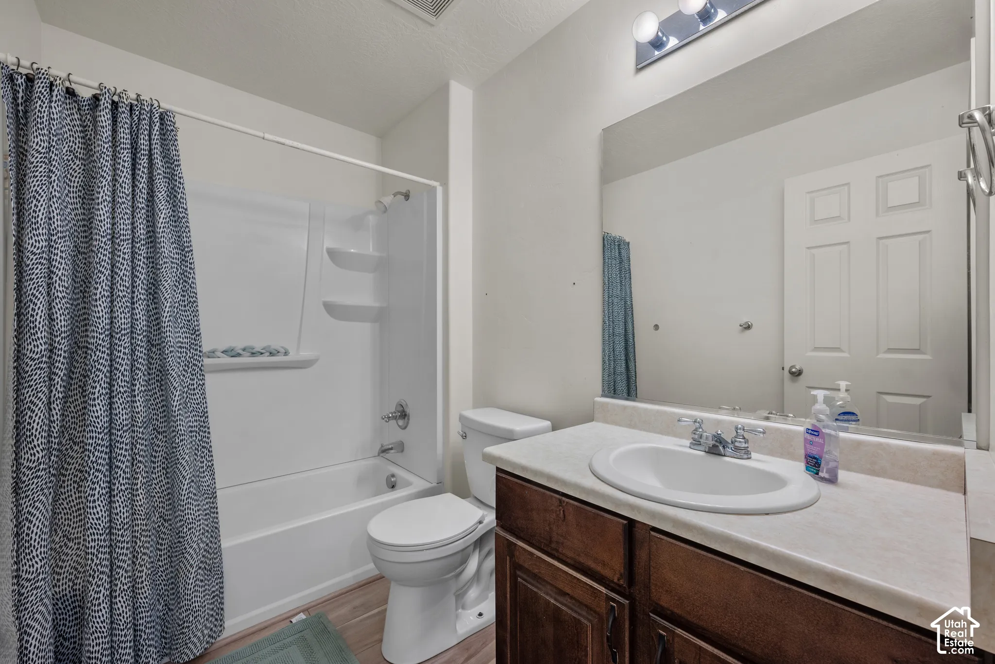 Bathroom featuring a wood-finish vanity, integrated countertop with an oval basin, chrome-finish dual-handle faucet, full-width wall mirror, and a tub-shower combination with built-in shelving