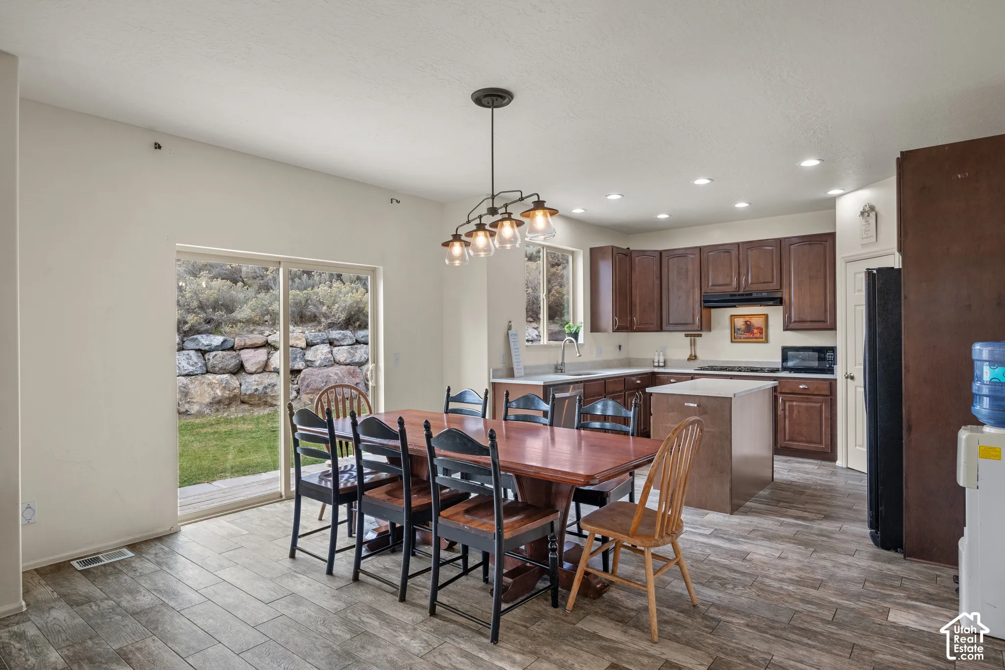 Kitchen featuring stained wood cabinetry, a central island with a quartz countertop, recessed lighting, wood-finish tile flooring, and a glass sliding door providing outdoor access