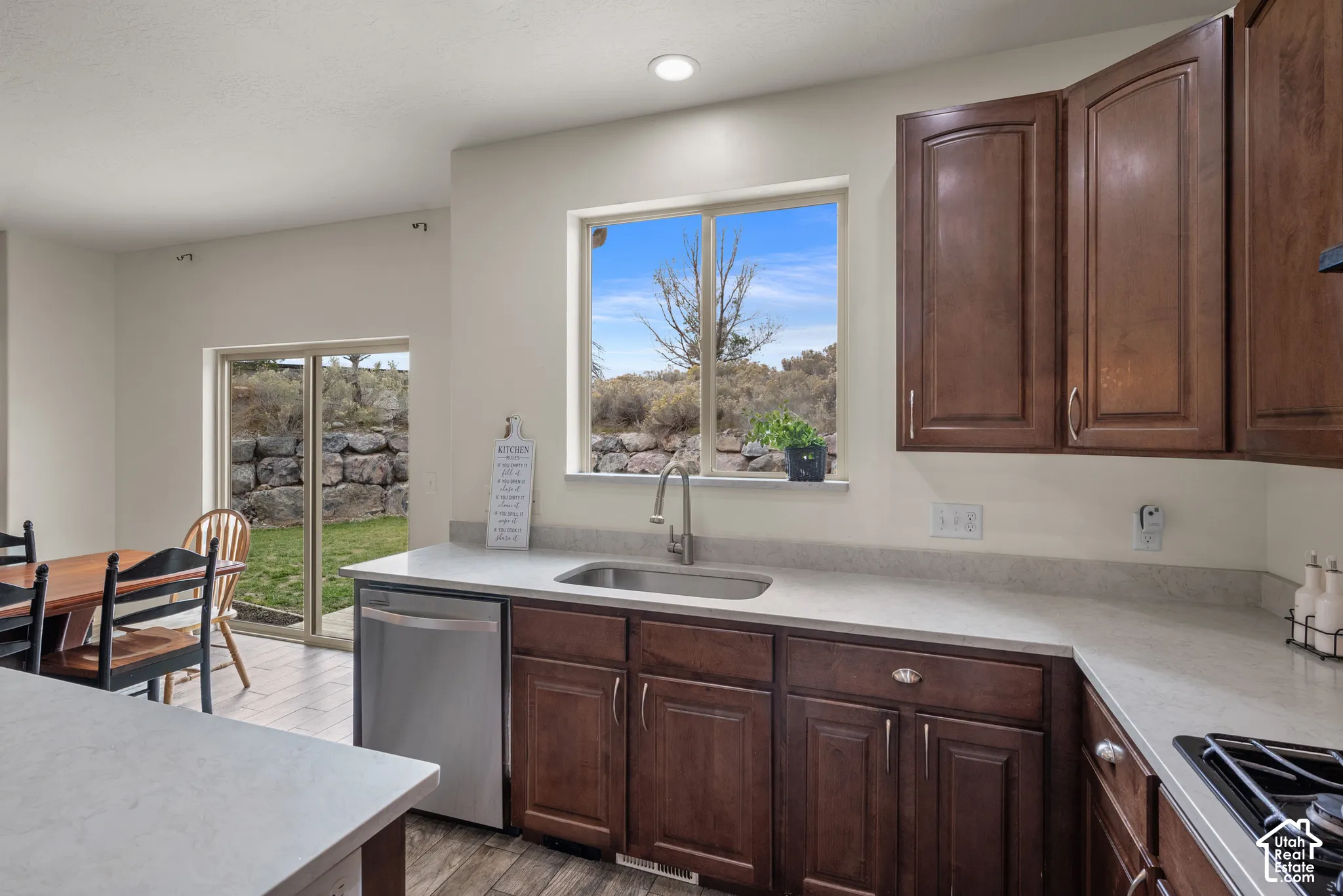 Kitchen featuring stained wood cabinetry, light-toned composite countertops, a stainless steel undermount sink with a gooseneck faucet, and wood-finish flooring