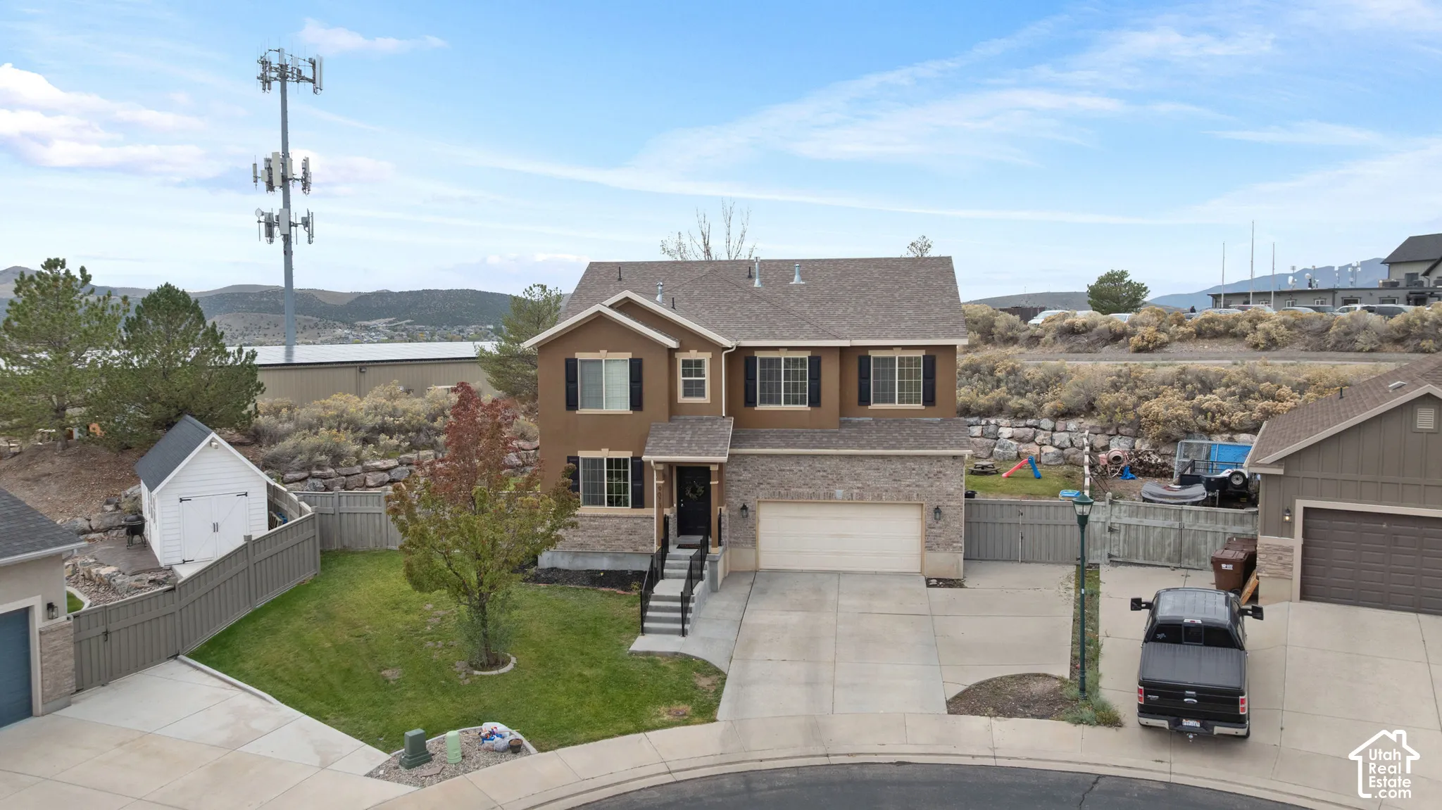 Two-story residence featuring stone and stucco exterior, attached two-car garage, concrete driveway, and detached storage shed