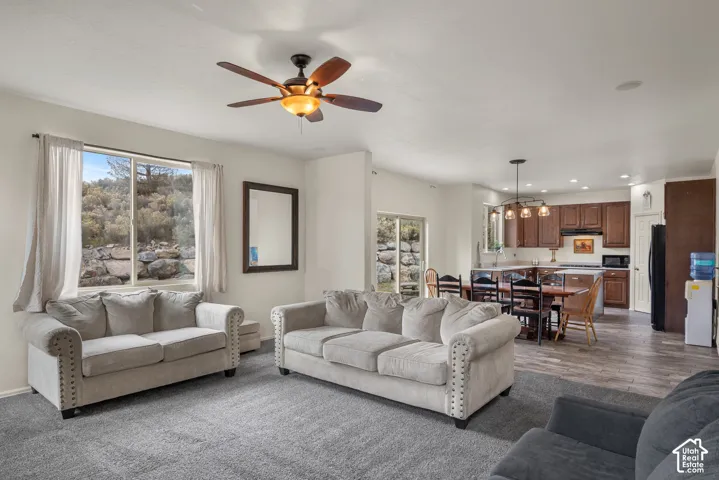 Open-concept living space featuring wood-finish flooring, a multi-blade ceiling fan, recessed lighting, and kitchen cabinetry with a decorative pendant fixture