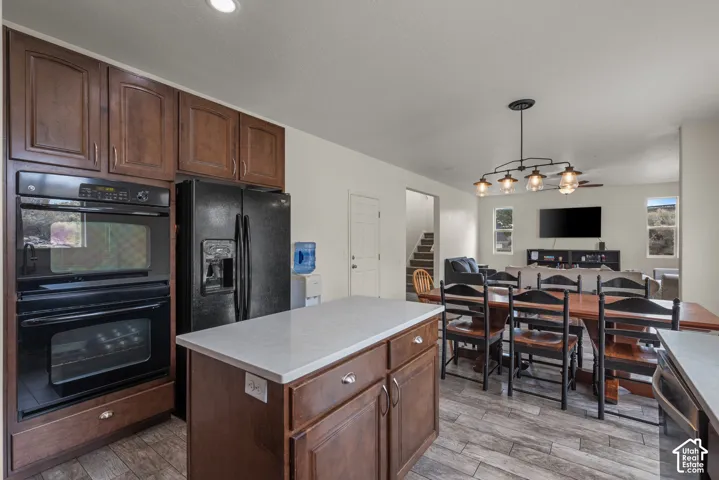 Kitchen featuring dark wood-finish cabinetry, a central island with a solid-surface countertop, built-in double ovens, and wood-finish flooring