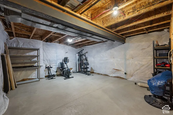 Unfinished lower level featuring concrete flooring, exposed wood joist ceilings, steel support beams, and plastic vapor barrier wall covering