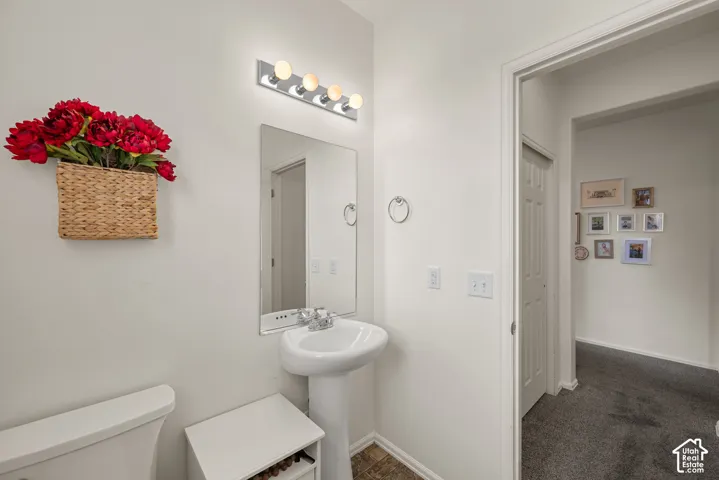 Powder room featuring a pedestal sink, frameless wall mirror, four-bulb vanity light fixture, and chrome hardware