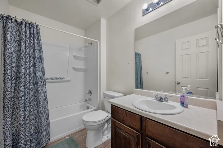 Bathroom featuring a wood-finish vanity, integrated countertop with an oval basin, chrome-finish dual-handle faucet, full-width wall mirror, and a tub-shower combination with built-in shelving