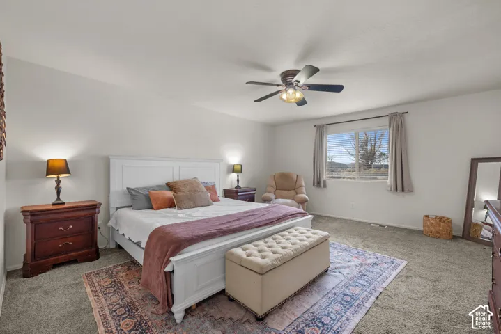 Neutral-toned bedroom featuring carpeting, a center-mounted ceiling fan with integrated lighting, and a large window