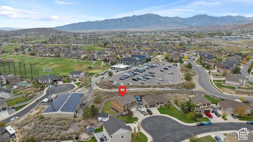 Aerial perspective of residential property featuring a multi-level structure, paved driveway, attached garage, and mountain backdrop