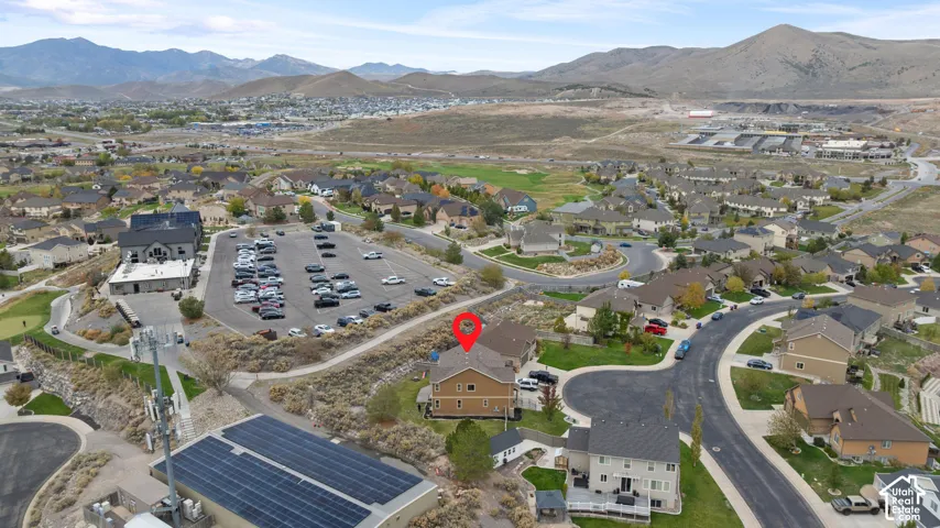 Aerial perspective of a multi-story residence featuring a shingled roof, neutral-toned siding, and a fenced yard, situated against a mountain backdrop