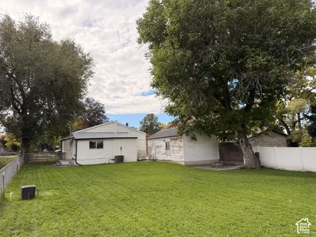 Expansive backyard featuring a manicured lawn, mature trees, white vinyl privacy fencing, and a detached outbuilding