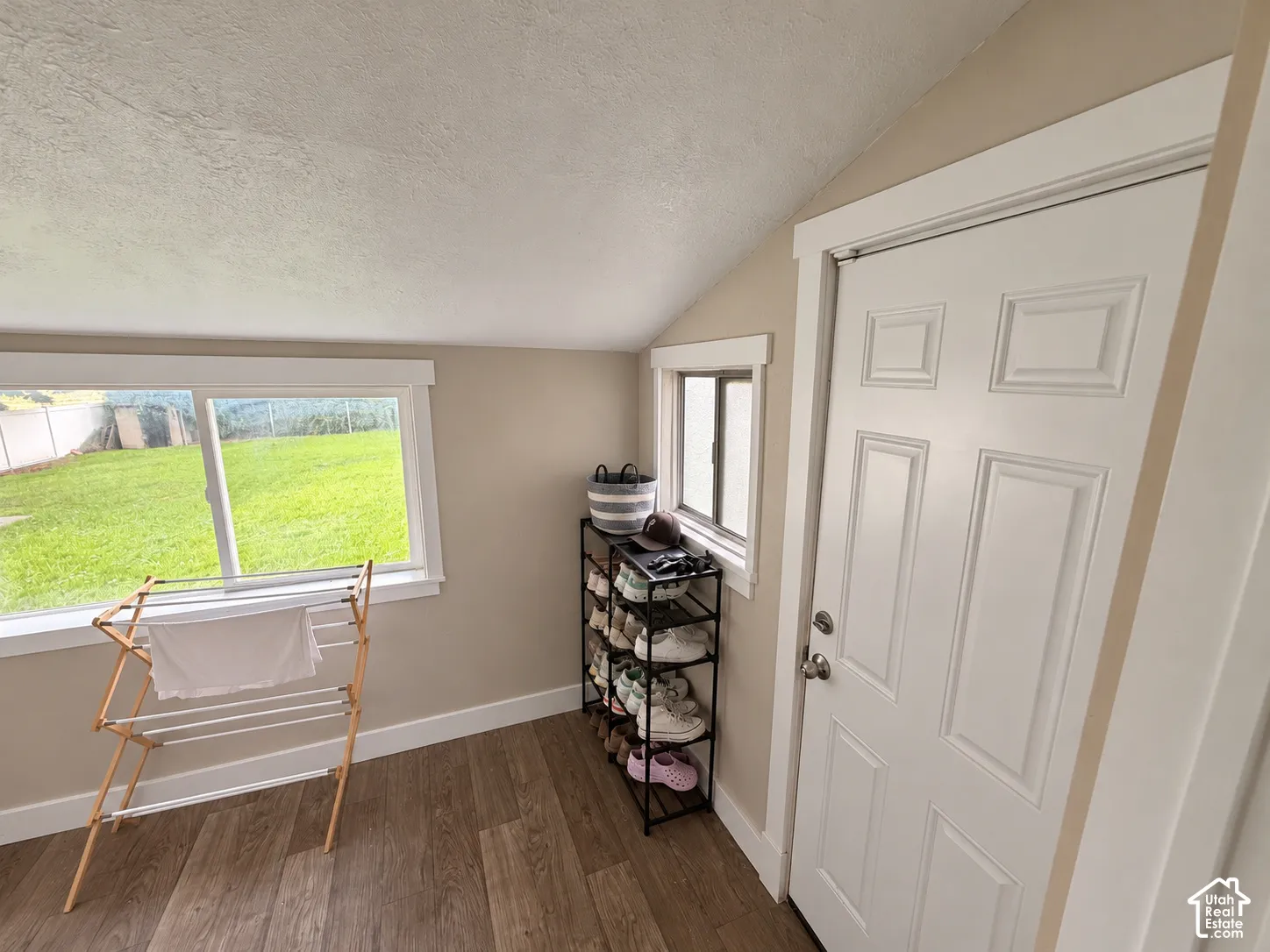 Sloped ceiling room featuring wood-finish flooring, white six-panel interior door, and dual sliding windows