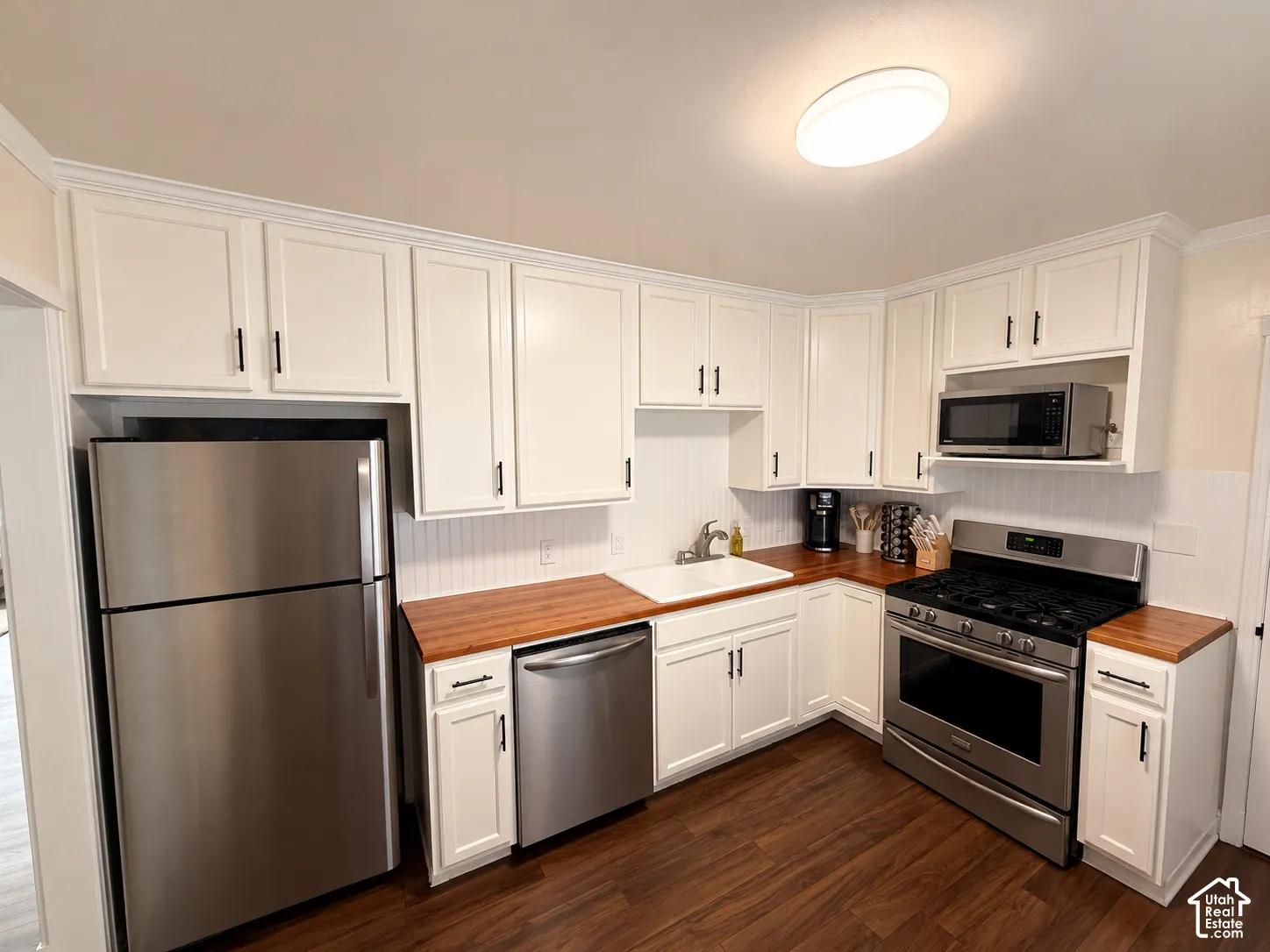 Kitchen featuring white shaker-style cabinetry, wood-finish countertops, stainless steel appliances, beadboard backsplash, and wood-finish flooring