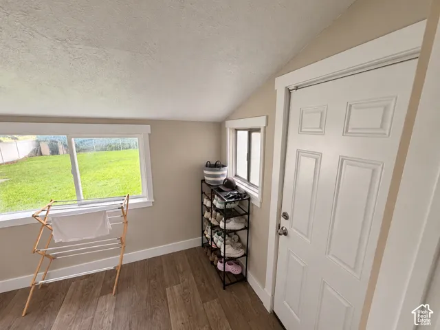 Sloped ceiling room featuring wood-finish flooring, white six-panel interior door, and dual sliding windows