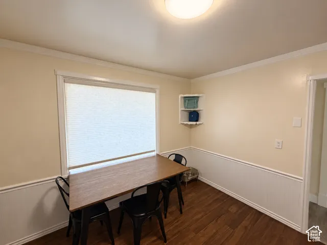 Room featuring white beadboard wainscoting, crown molding, wood-finish flooring, a built-in corner shelf, and a large window with a pleated shade