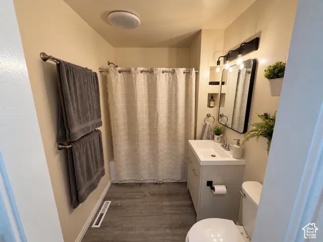Bathroom featuring wood-finish flooring, vanity with an integrated sink, matte black vanity lighting, and recessed wall shelving