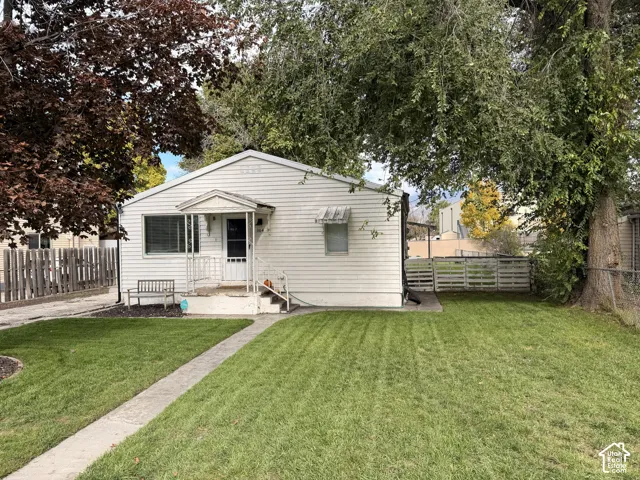 Exterior featuring light-colored horizontal siding, a gabled roofline, a front porch with metal railings, a concrete walkway, and a fenced yard with mature trees