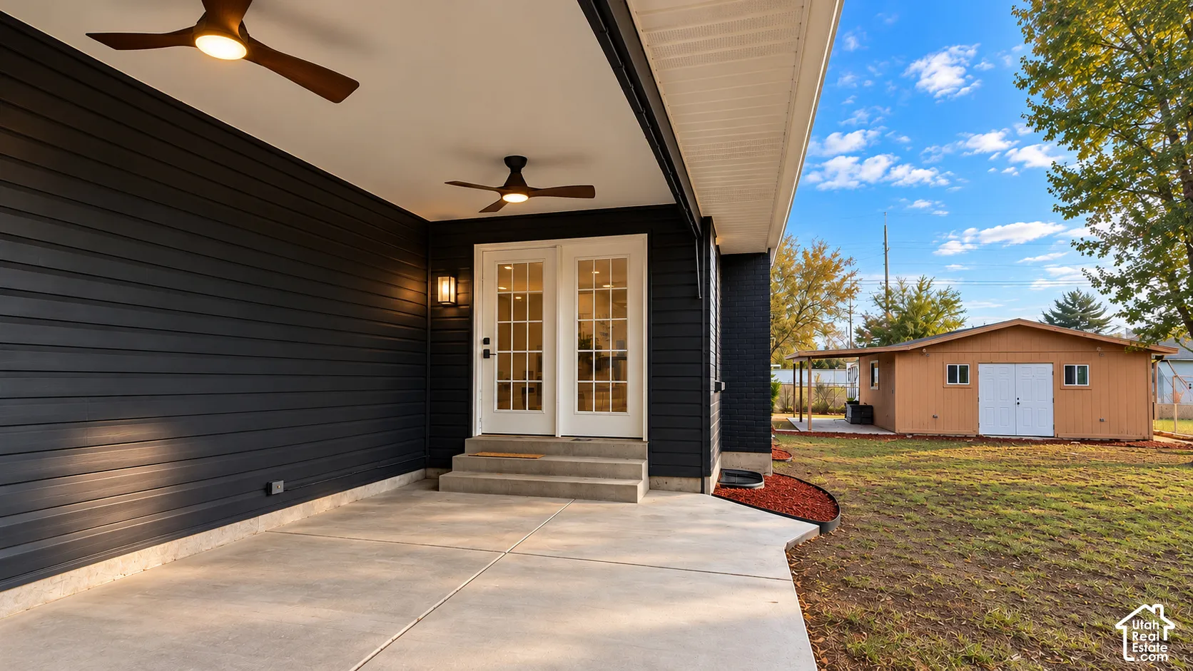 Covered patio featuring dark horizontal siding, two ceiling fans with integrated lighting, concrete flooring, and double glass-paneled doors