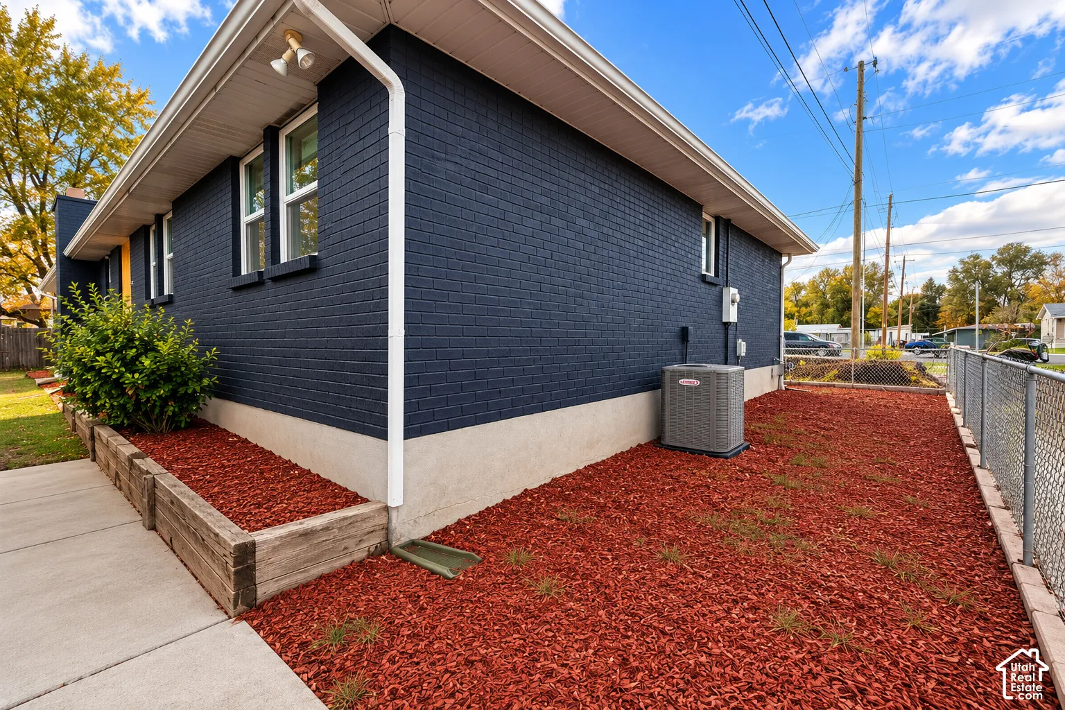 Dark navy brick exterior featuring white trim, concrete foundation, timber-framed planting beds, and external HVAC unit