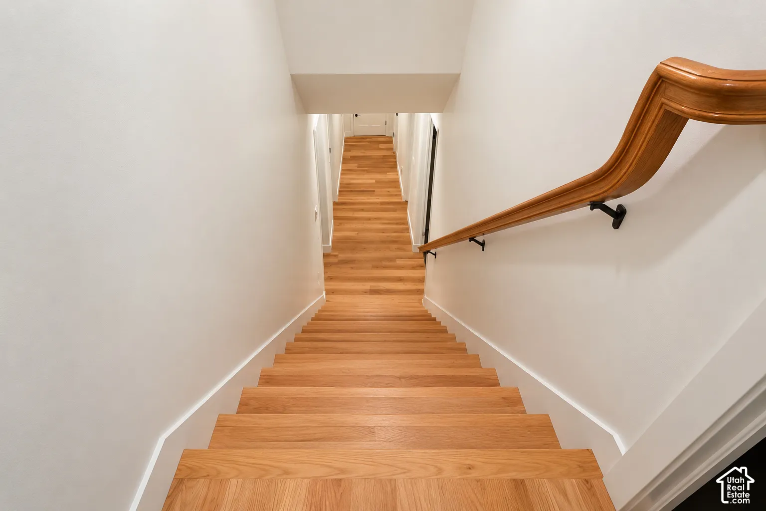 Staircase featuring wood-finish treads and landing, complemented by a contoured wood handrail with matte black metal brackets