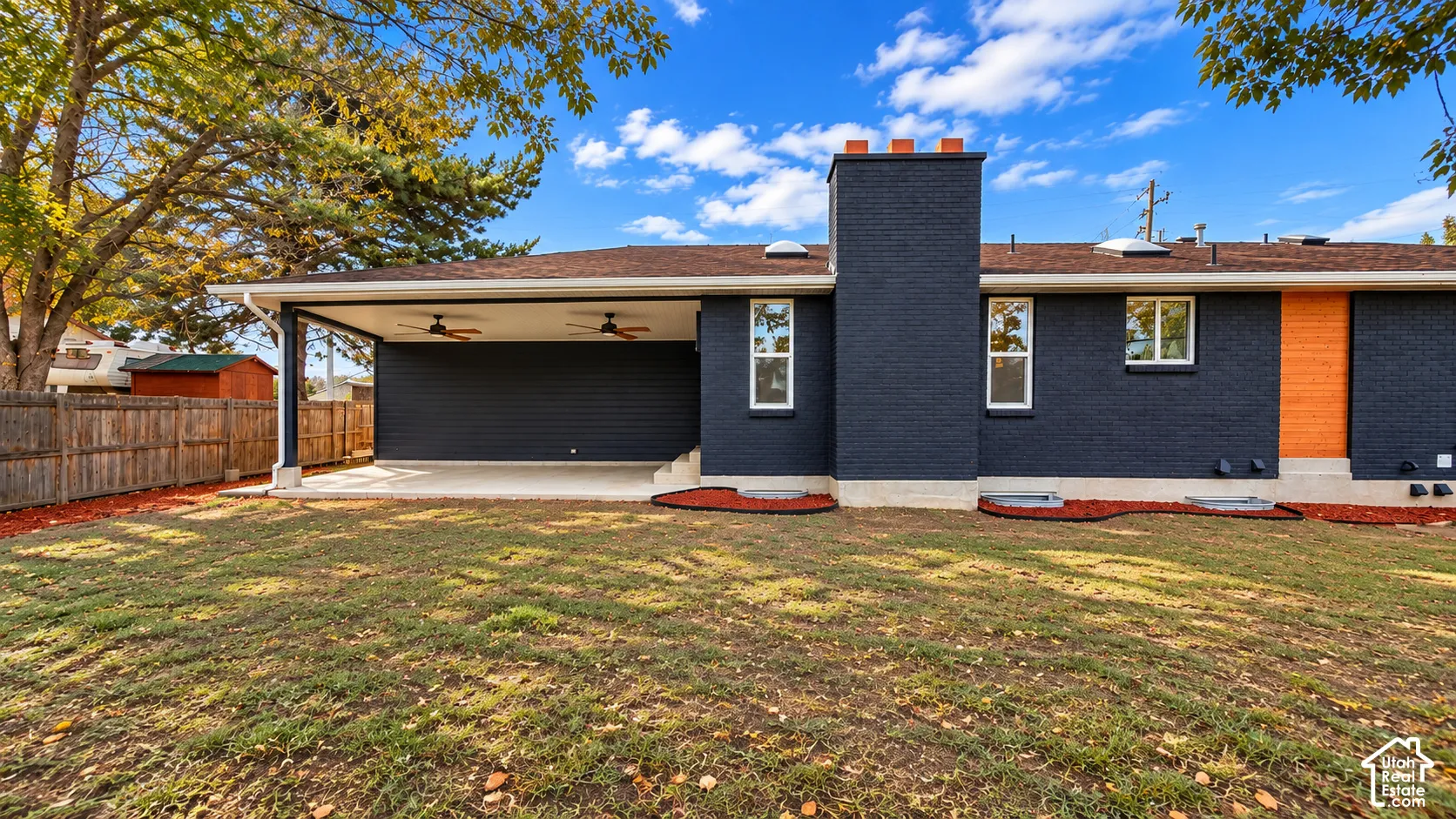 Exterior featuring dark painted brick, a covered patio with ceiling fans, a central chimney, and a fenced backyard