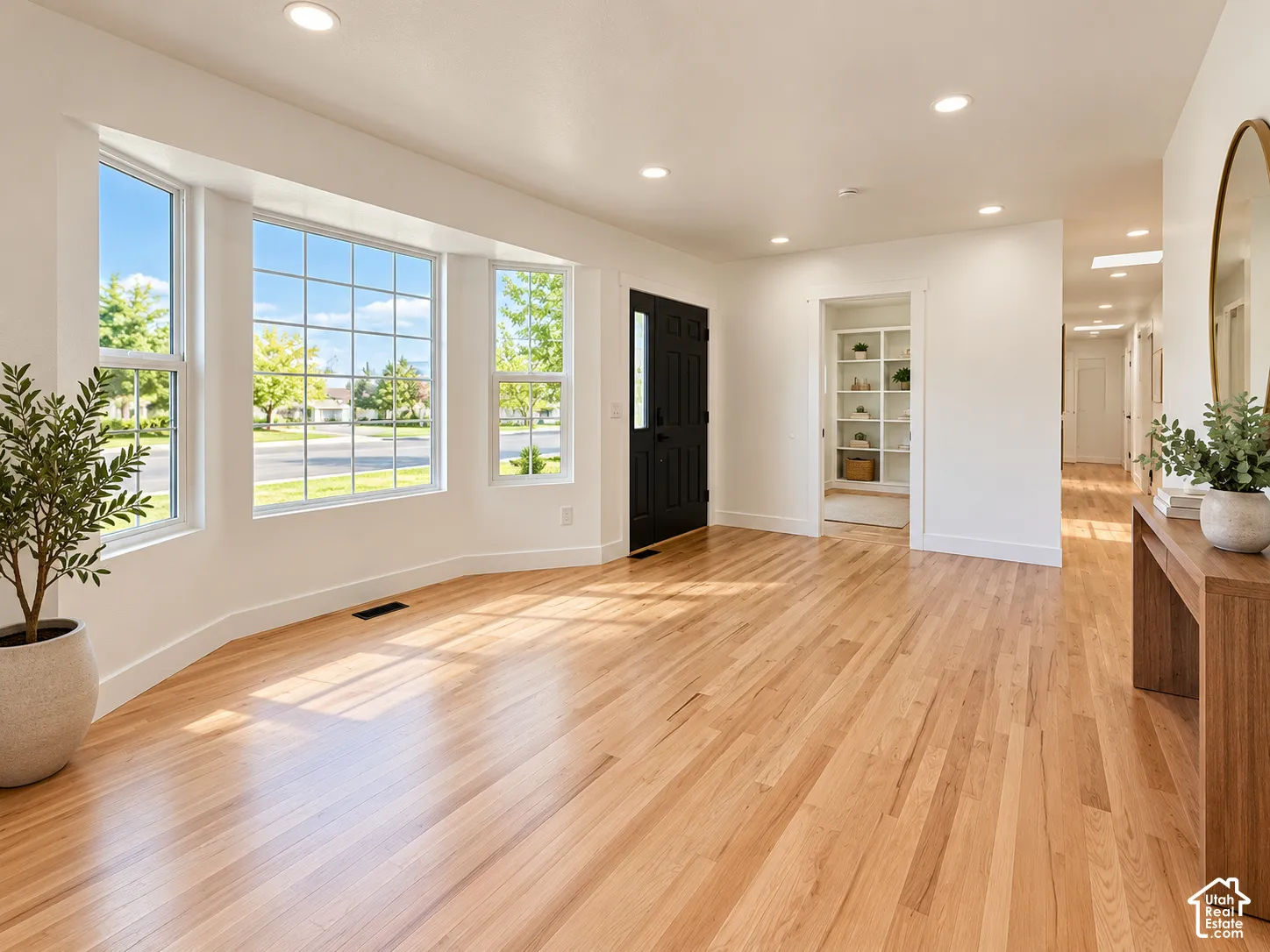 Living area featuring wood-finish flooring, a multi-pane bay window, recessed ceiling lighting, and a contrasting black paneled front door