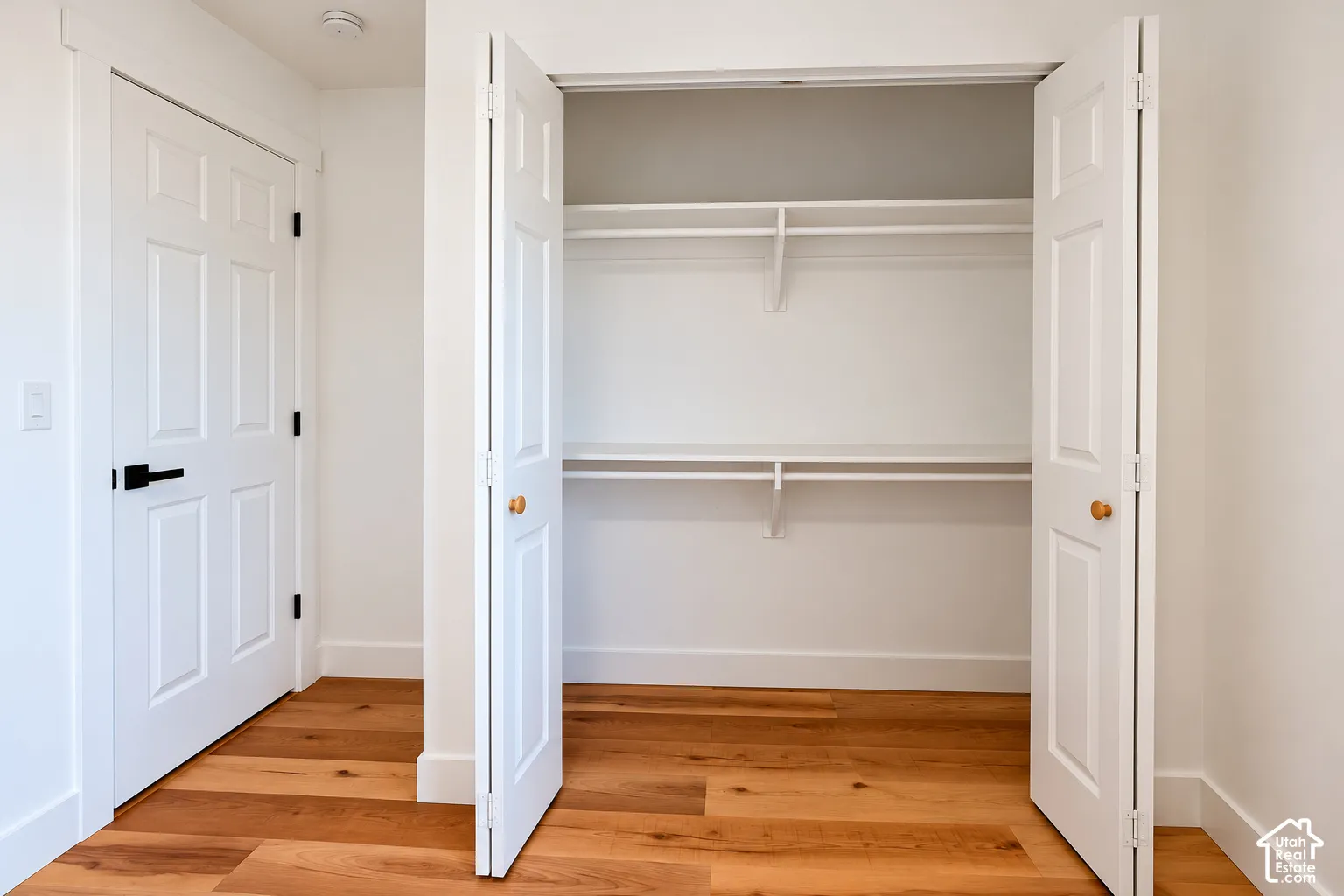 Reach-in closet featuring dual bifold doors, integrated shelving, wood-finish flooring, and a six-panel door with matte black hardware